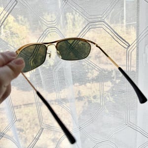 Peut inclure: Lunettes de soleil &agrave; monture en m&eacute;tal dor&eacute; avec des verres teint&eacute;s vert fonc&eacute; et des branches fines en fil m&eacute;tallique dot&eacute;es d'embouts en plastique noir. Le pont comporte des plaquettes r&eacute;glables pour un ajustement pr&eacute;cis.