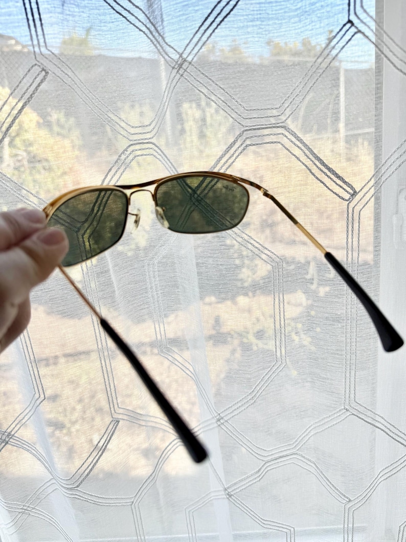 Peut inclure: Lunettes de soleil &agrave; monture en m&eacute;tal dor&eacute; avec des verres teint&eacute;s vert fonc&eacute; et des branches fines en fil m&eacute;tallique dot&eacute;es d'embouts en plastique noir. Le pont comporte des plaquettes r&eacute;glables pour un ajustement pr&eacute;cis.