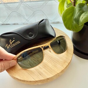 Peut inclure: Lunettes de soleil &agrave; monture en m&eacute;tal dor&eacute; avec verres vert fonc&eacute; et logo Ray-Ban sur le verre. Inclut un &eacute;tui de protection en similicuir noir avec le texte Ray-Ban SUNGLASSES by BAUSCH & LOMB imprim&eacute; en dor&eacute; sur le rabat avant.