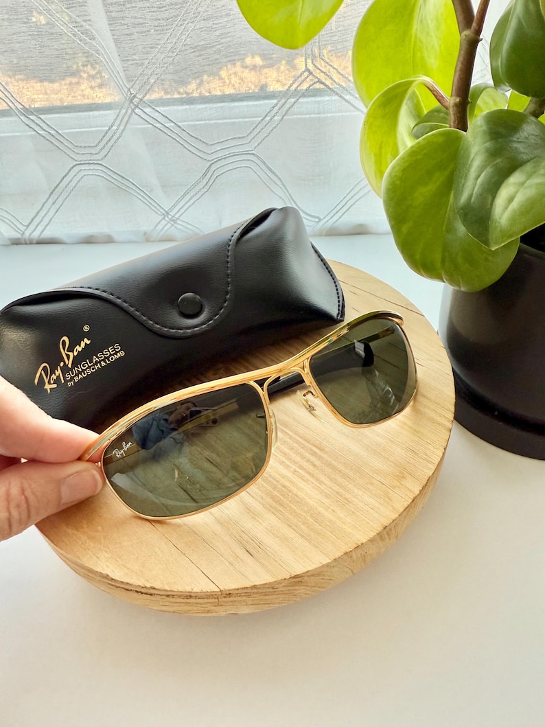 Peut inclure: Lunettes de soleil &agrave; monture en m&eacute;tal dor&eacute; avec verres vert fonc&eacute; et logo Ray-Ban sur le verre. Inclut un &eacute;tui de protection en similicuir noir avec le texte Ray-Ban SUNGLASSES by BAUSCH & LOMB imprim&eacute; en dor&eacute; sur le rabat avant.