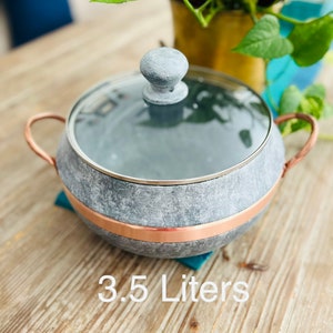 K&ouml;nnte beinhalten: Ein grauer Steintopf mit Kupferrand und Glasdeckel. Der Topf hat einen Knopf auf dem Deckel und zwei Kupfergriffe. Der Topf steht auf einer Holzoberfl&auml;che. 3,5 Liter.