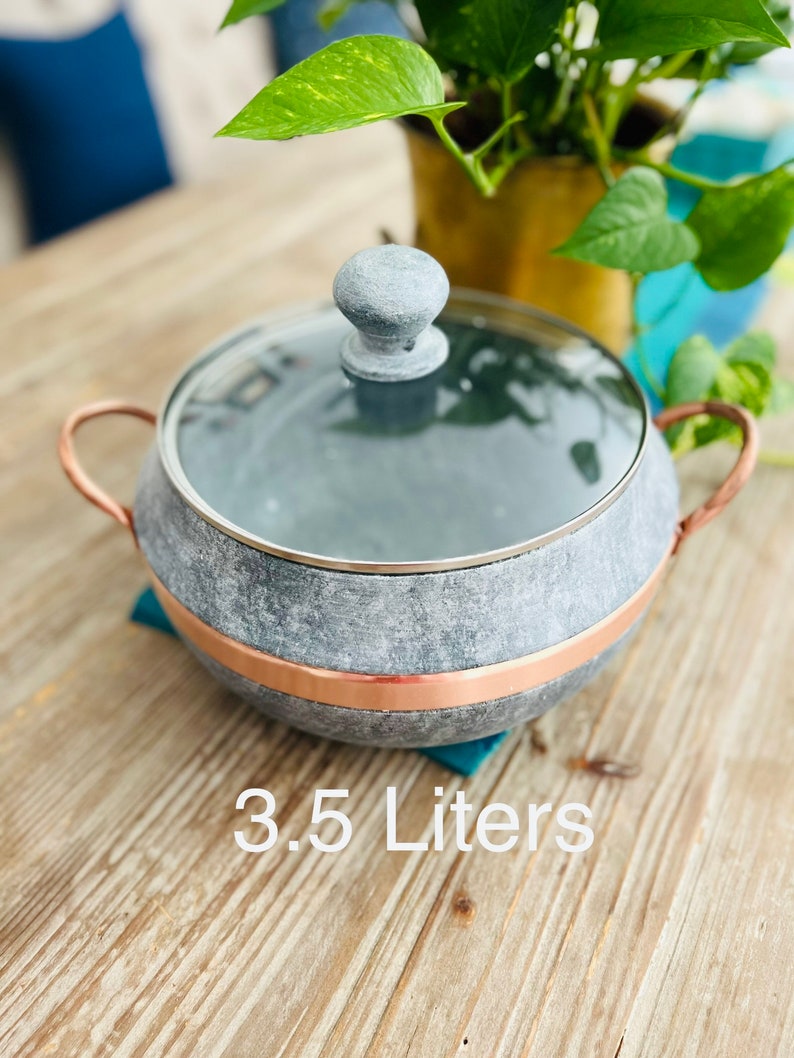 K&ouml;nnte beinhalten: Ein grauer Steintopf mit Kupferrand und Glasdeckel. Der Topf hat einen Knopf auf dem Deckel und zwei Kupfergriffe. Der Topf steht auf einer Holzoberfl&auml;che. 3,5 Liter.