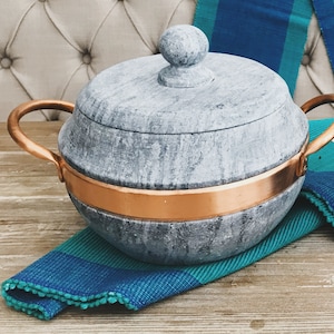May include: A round gray soapstone pot with a copper band around the rim and a copper handle. The pot has a lid with a round knob on top.