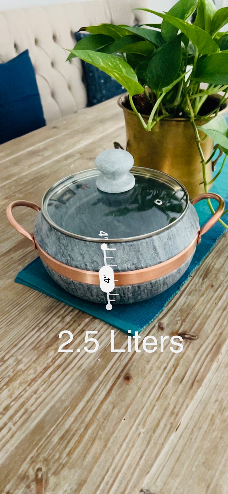 K&ouml;nnte beinhalten: Ein grauer Specksteintopf mit Kupferrand und Glasdeckel. Der Topf hat einen Holzgriff und ein Lineal an der Seite, das "4 Zoll" anzeigt. Der Topf steht auf einem blauen Untersetzer und einem Holztisch. Der Text "2,5 Liter" ist unter dem Topf aufgedruckt.
