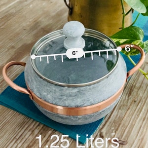 "A handcrafted soapstone pot with a transparent glass lid, showcasing its smooth, natural stone finish. The sturdy pot is designed for even heat retention, while the glass lid allows for easy monitoring of the cooking process."