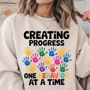 May include: A white ceramic mug with a black handle and the text "But First, Coffee" in a bold, black font. The mug is set against a blurred background, highlighting its clean design.