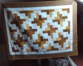 May include: A handmade quilt with a geometric pattern. The quilt features a white centre with a repeating pattern of brown and tan blocks. It has a brown border and a white inner border. The quilt is likely used for bedding or decoration.