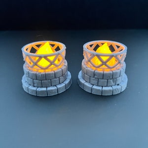 May include: Two small, white, 3D printed candle holders with a brick-like base and a wire cage design. Each holder has a small, yellow LED candle inside.