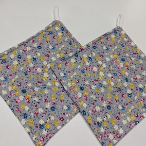 Könnte beinhalten: Zwei graue Topflappen aus Stoff mit einem Blumenmuster in den Farben Rosa, Gelb und Blau.