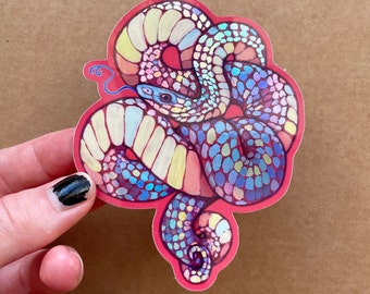May include: A vibrant sticker with a snake illustration. The snake is rendered in a palette of blues, purples, yellows, and pinks, outlined in red. The snake's tongue is blue, and its eye is light blue. The sticker has a red border.