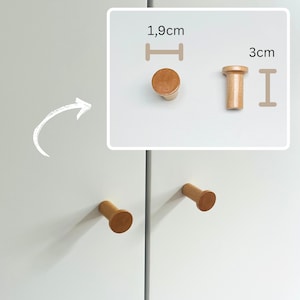 May include: Wooden cabinet knobs in a light brown color. One knob is 1.9cm in diameter, and the other is 3cm tall. The knobs are cylindrical with a flat top and are mounted on a white cabinet door. The image shows the knobs in different positions.