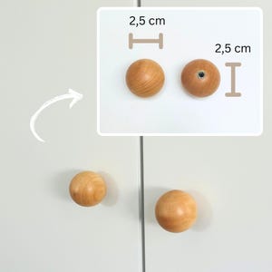 May include: Wooden cabinet knobs with a spherical design. The knobs are light brown and measure 1 inch in diameter. One knob has a pre-drilled hole for installation. The knobs are shown on a white cabinet door.