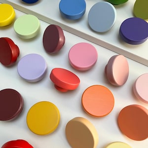 Może przedstawiać: Kolekcja kolorowych, okrągłych gałek do szafek w różnych odcieniach, w tym niebieskim, zielonym, żółtym, różowym i pomarańczowym. Gałki mają prosty, nowoczesny design i są ułożone na białej powierzchni. Idealne do dodania koloru.