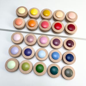 May include: A collection of twenty-one wooden cabinet knobs with a natural wood base and a variety of colorful, round, painted tops. Colors include yellow, orange, pink, red, purple, blue, green, and neutral tones.