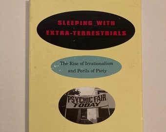 May include: A yellow book cover with the title "Sleeping with Extra-Terrestrials" and the subtitle "The Rise of Irrationalism and Perils of Piety". The cover also features a black and white photo of a sign that reads "Psychic Fair Today". The author's name, Wendy Kaminer, is printed in black below the photo. A quote from Katha Pollitt is printed at the bottom of the cover.