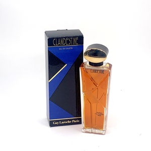 Può includere: Un flacone di Clandestine Eau de Toilette di Guy Laroche Paris. Il flacone è in vetro trasparente con un tappo dorato e un'etichetta dorata con il nome della fragranza. La scatola è blu e nera con il nome della fragranza e del designer.