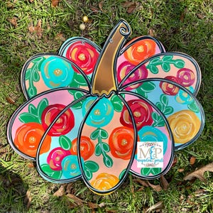 May include: A pink and blue pumpkin with a floral design. The pumpkin is painted with bright colors and has a black outline. The text "MP Magnolia Pearls" is in the bottom right corner.