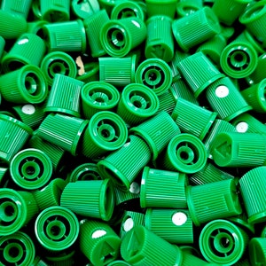 May include: A close-up view of a pile of green spray paint caps. The caps are all the same size and shape, and they have a small hole in the center. The caps are made of plastic and have a textured surface.