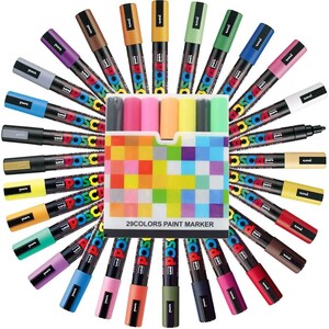 May include: A set of 29 colorful paint markers arranged in a circle around a box with a checkered pattern. The box has the text "29COLORS PAINT MARKER" printed on it. The markers are all the same size and shape, and they have a variety of colors, including red, blue, green, yellow, and purple.