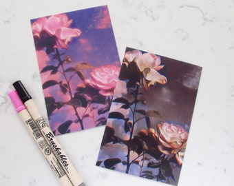 May include: Two postcards with a pink and white rose illustration against a purple and blue sky background.