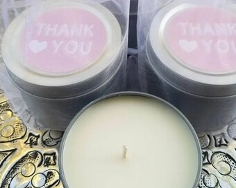 May include: A set of three small, silver tin candle jars with a white candle inside each jar. The jars have pink lids with the words "Thank You" and a heart printed on them.