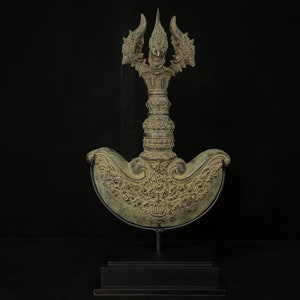 Könnte beinhalten: Eine Bronzeskulptur einer stilisierten, verzierten, dreiköpfigen Kreatur mit einer sichelförmigen Basis. Die Skulptur steht auf einem schwarzen Sockel.