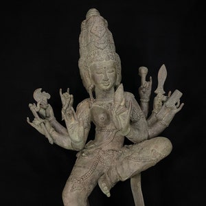 Puede incluir: Una estatua de bronce de una deidad con múltiples brazos, cada uno sosteniendo un objeto diferente. La deidad está de pie en una pose dinámica con una corona en la cabeza.