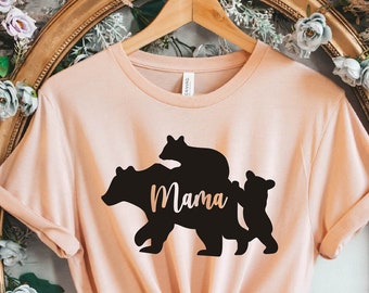 May include: A light pink t-shirt with a black silhouette of a mama bear and two cubs. The text "Mama" is written on the bear's belly.