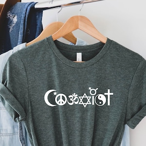 May include: A dark green t-shirt with the word "Coexist" printed in white. The word is surrounded by symbols representing different religions, including a crescent moon, a peace sign, an Om symbol, a Star of David, a yin-yang symbol, and a cross.
