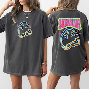 May include: A dark gray oversized t-shirt with a graphic of a distorted smiley face with the word "NIRVANA" in pink letters above it.