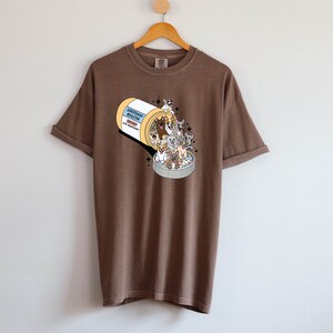 May include: A brown t-shirt with a graphic of a pill bottle overflowing with cartoon dogs. The pill bottle label reads "Serotonin Booster".