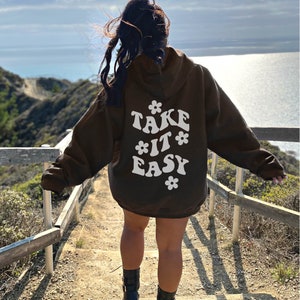May include: A brown hoodie with a white graphic on the back that says "TAKE IT EASY" with stylized flowers around the text.