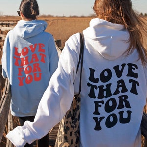 May include: Two people wearing hoodies with the text "LOVE THAT FOR YOU" printed on the back. One hoodie is light blue with red text, and the other is white with black text.