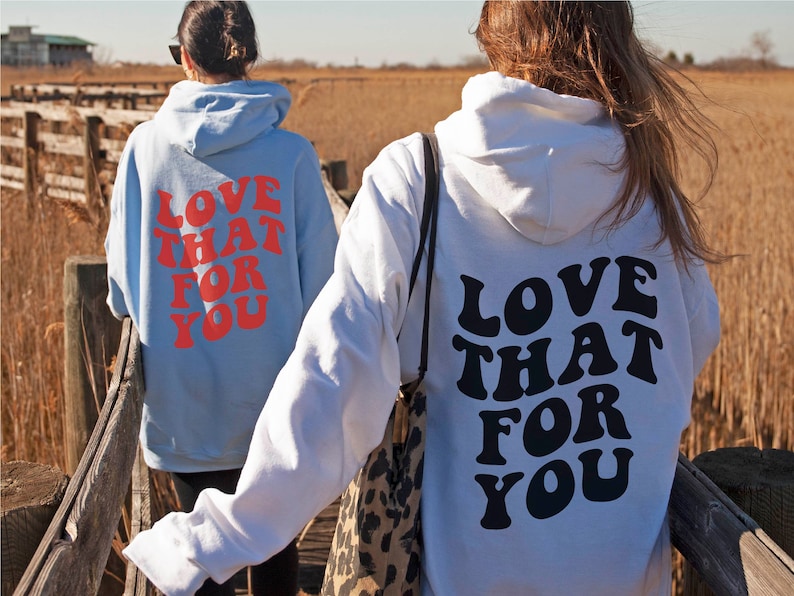 May include: Two people wearing hoodies with the text "LOVE THAT FOR YOU" printed on the back. One hoodie is light blue with red text, and the other is white with black text.