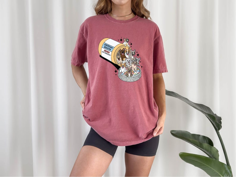 May include: A maroon t-shirt with a graphic of a pill bottle overflowing with cartoon cats. The text on the pill bottle reads "Catnip Mood Booster".