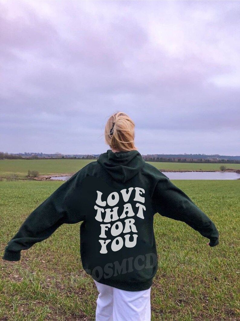 May include: A dark green hoodie with the text "LOVE THAT FOR YOU" in white on the back. The hoodie is worn by a person standing in a field.