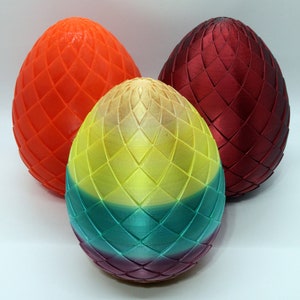 May include: Three decorative, egg-shaped objects with a diamond pattern. The eggs are in shades of orange, red, and a gradient of yellow, green, and purple. The objects are likely 3D-printed and have a textured surface.