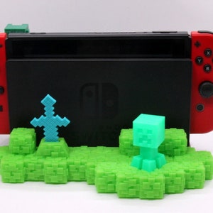 May include: A green Minecraft-themed stand for a Nintendo Switch console. The stand features a green block with a sword and a Creeper figure.