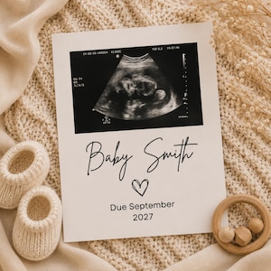 May include: A white rectangular announcement card featuring a black and white ultrasound image at the top. Below the image, the text reads Baby Smith in a script font, followed by a small heart icon and the text Due September 2027.