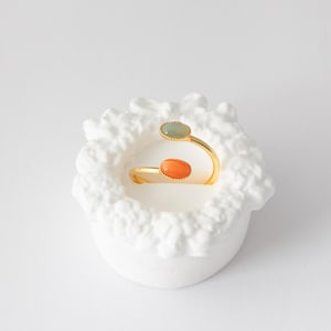 May include: A gold ring with two oval-shaped stones. The larger stone is a light green color, and the smaller stone is a light orange color.