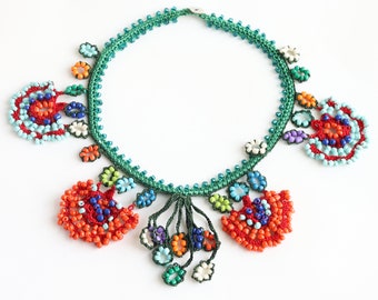 May include: A green crocheted necklace with colorful beaded flowers. The necklace features a variety of colors, including red, orange, blue, green, and white.