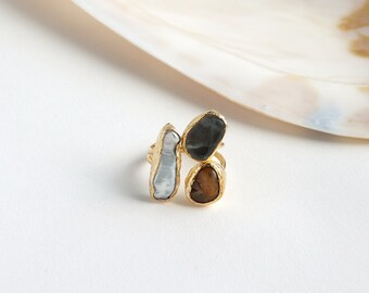 May include: Gold ring with three stones: a white pearl, a black stone, and a brown stone.