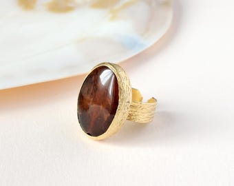 May include: A gold ring with a large oval-shaped brown stone set in the center. The ring band is textured and has a hammered finish.