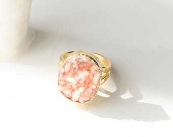 May include: A gold ring featuring a large, oval-shaped pink crystal. The crystal has a rough, textured surface.