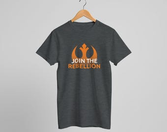 May include: Dark gray t-shirt with an orange graphic of a stylized emblem and the words "JOIN THE REBELLION". The shirt is hanging on a wooden hanger against a light gray background.