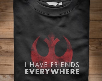 May include: Black t-shirt with a distressed red graphic and the text "I HAVE FRIENDS EVERYWHERE" in white. The graphic is a stylized symbol. The shirt is folded on a wooden surface.