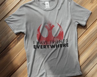 May include: A light gray t-shirt featuring a distressed red symbol and the text "I HAVE FRIENDS EVERYWHERE" in black. The shirt is made of a soft material and has a crew neck.