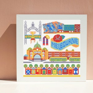 Op de afbeelding: Een kleurrijk kruissteekpatroon met iconische bezienswaardigheden van Melbourne, waaronder het Royal Exhibition Building, trams, strandhuisjes en het woord "MELBOURNE" op een banner.