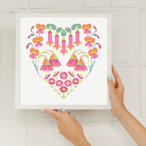 Puede incluir: Un patrón de punto de cruz de un diseño floral en forma de corazón con flores rosas, naranjas y verdes. El diseño está enmarcado en un marco blanco.