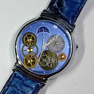 Peut inclure: Une montre argentée avec un cadran bleu et des engrenages apparents. La montre a un bracelet en cuir bleu avec un motif crocodile.